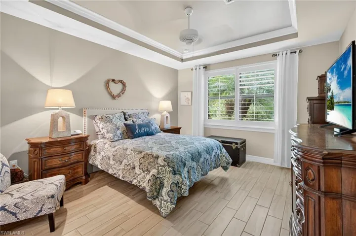 Bedroom with light wood-style flooring, ceiling fan, and a raised ceiling