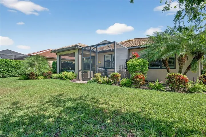 Rear view of house with a lanai, a lawn, a tiled roof, and stucco siding