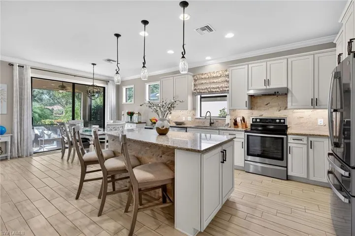 Kitchen featuring stainless steel appliances, crown molding, backsplash, a kitchen bar, and light stone counters