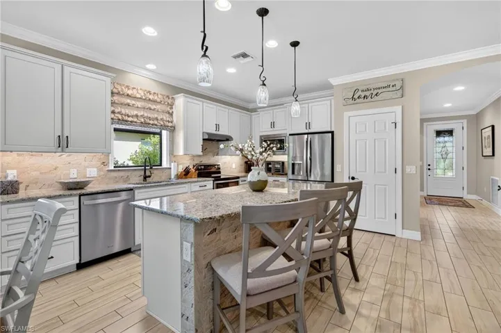 Kitchen featuring wood tiled floors, backsplash, hanging light fixtures, a kitchen bar, and ornamental molding