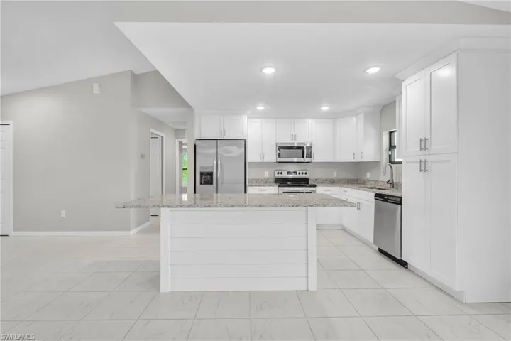 Kitchen with marble finish floor, a sink, a center island, stainless steel appliances, and white cabinets