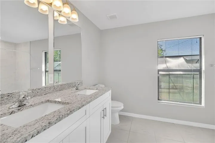 Full bath with marble finish floor, toilet, baseboards, and a sink
