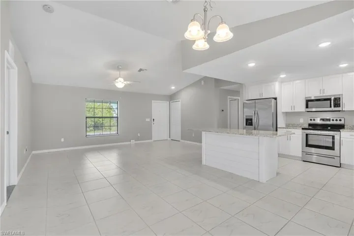 Kitchen with lofted ceiling, stainless steel appliances, white cabinetry, open floor plan, and a center island