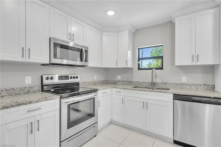 Kitchen with light stone countertops, appliances with stainless steel finishes, marble finish floor, white cabinetry, and a sink