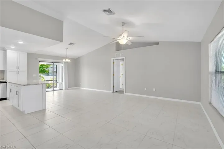 Unfurnished living room featuring visible vents, ceiling fan with notable chandelier, baseboards, and vaulted ceiling