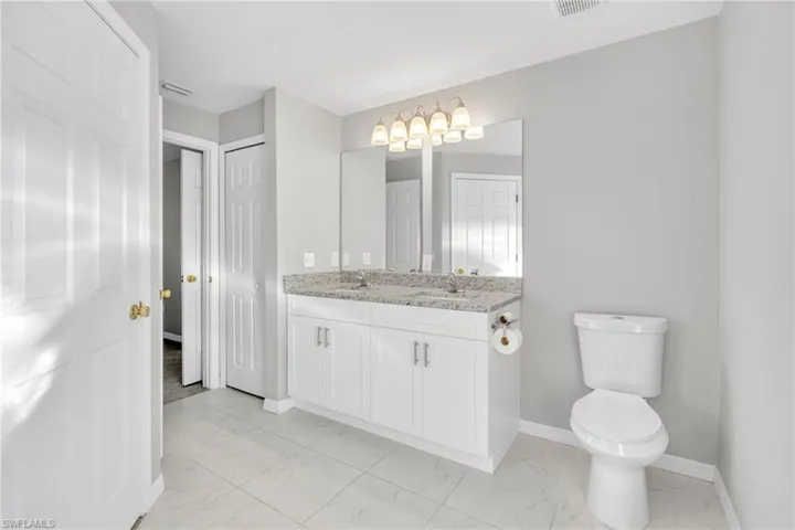 Bathroom with baseboards, toilet, double vanity, marble finish floor, and a sink