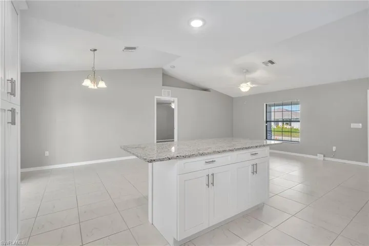 Kitchen featuring visible vents, ceiling fan with notable chandelier, white cabinets, and lofted ceiling