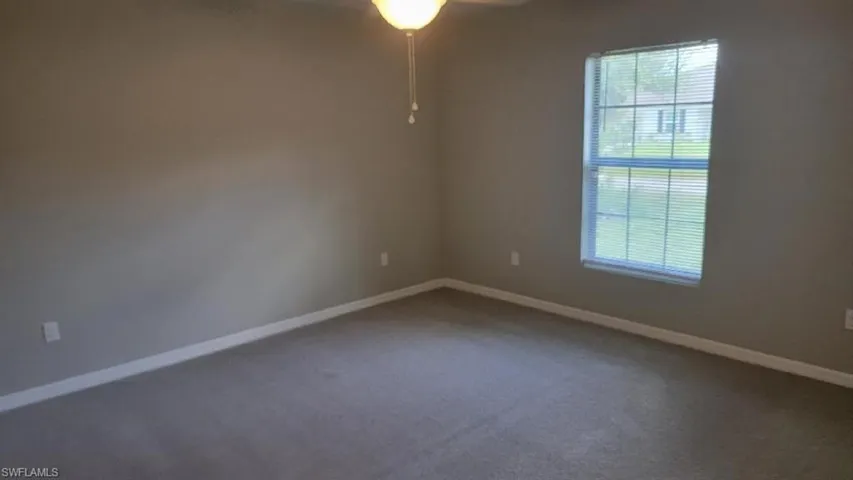 Carpeted empty room with ceiling fan and baseboards