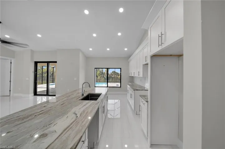 Kitchen with a sink, recessed lighting, white cabinets, light stone counters, and baseboards