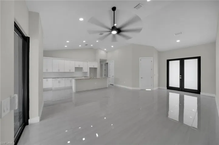 Unfurnished living room with vaulted ceiling, french doors, a ceiling fan, light tile patterned floors, and baseboards