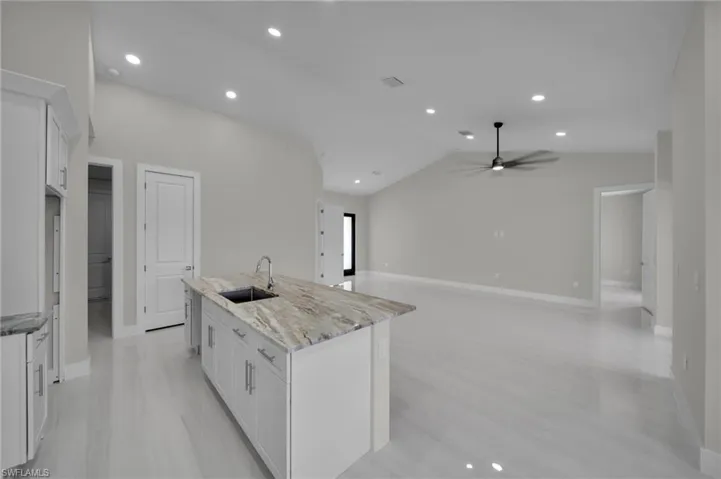 Kitchen featuring a sink, a center island with sink, white cabinetry, baseboards, and light stone counters