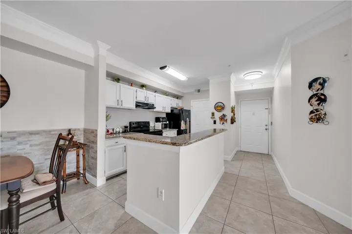 Kitchen featuring dark stone countertops, black appliances, white cabinets, light tile patterned floors, and crown molding