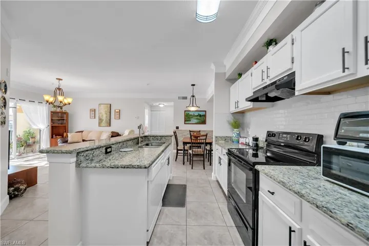 Kitchen with electric range, ornamental molding, white cabinetry, light stone counters, and a kitchen island with sink
