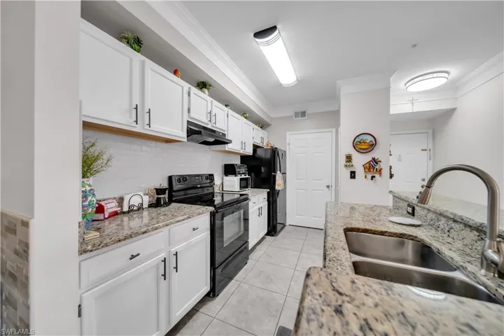 Kitchen with black appliances, ornamental molding, white cabinets, light stone countertops, and decorative backsplash