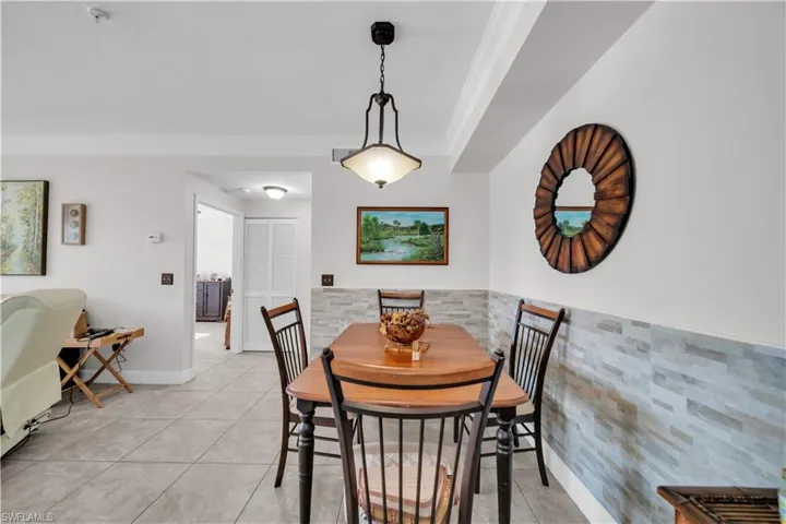 Dining space with crown molding, light tile patterned floors, and a wainscoted wall