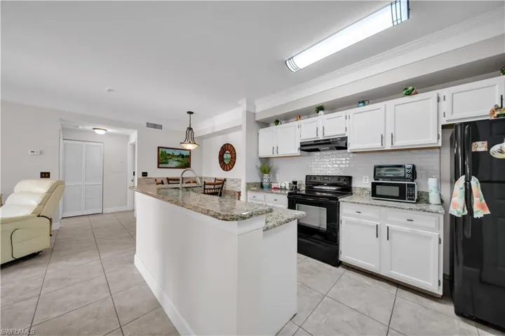 Kitchen featuring white cabinets, black appliances, light tile patterned floors, ornamental molding, and pendant lighting
