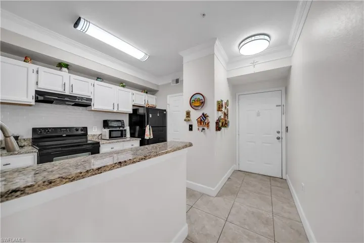 Kitchen featuring white cabinets, black appliances, crown molding, light stone countertops, and decorative backsplash