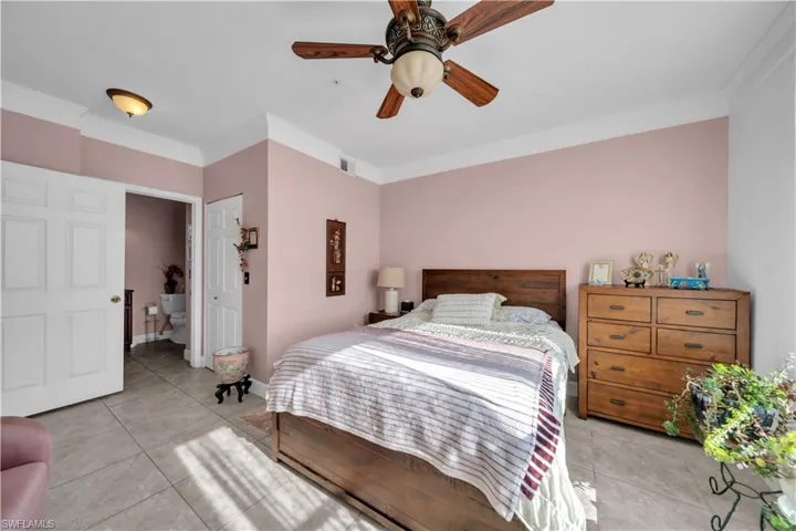 Bedroom featuring ornamental molding, light tile patterned floors, a ceiling fan, and ensuite bath