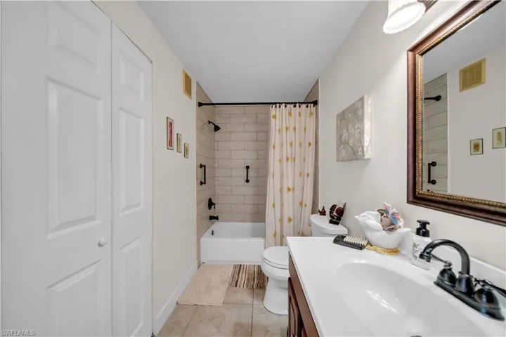 Full bathroom with vanity, shower / bathtub combination with curtain, light tile patterned flooring, and a closet