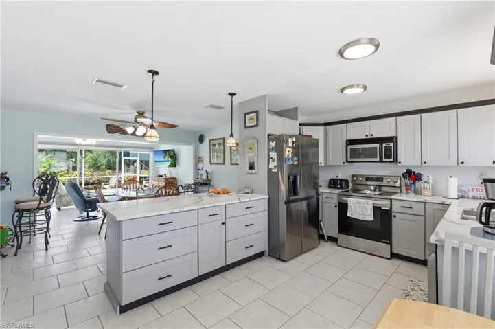 Kitchen with stainless steel appliances, a peninsula, ceiling fan, gray cabinets, and light stone countertops