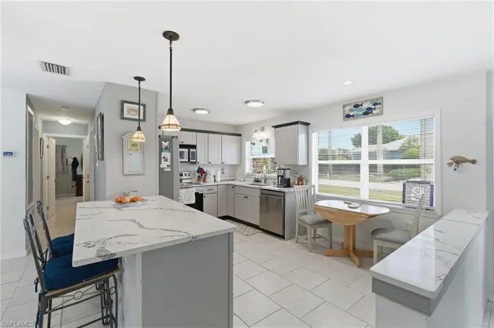 Kitchen with a center island, gray cabinets, light stone counters, stainless steel appliances, and a breakfast bar