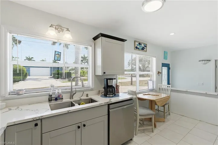 Kitchen featuring dishwasher, light stone counters, and healthy amount of natural light