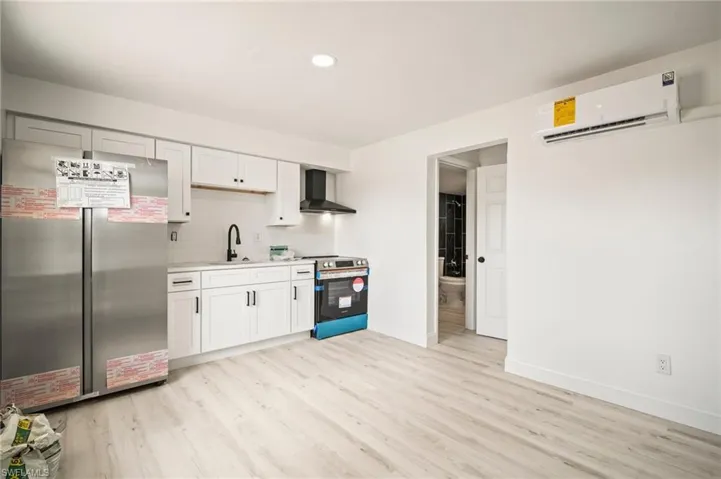 Kitchen with appliances with stainless steel finishes, wall chimney exhaust hood, an AC wall unit, light countertops, and light wood-style floors