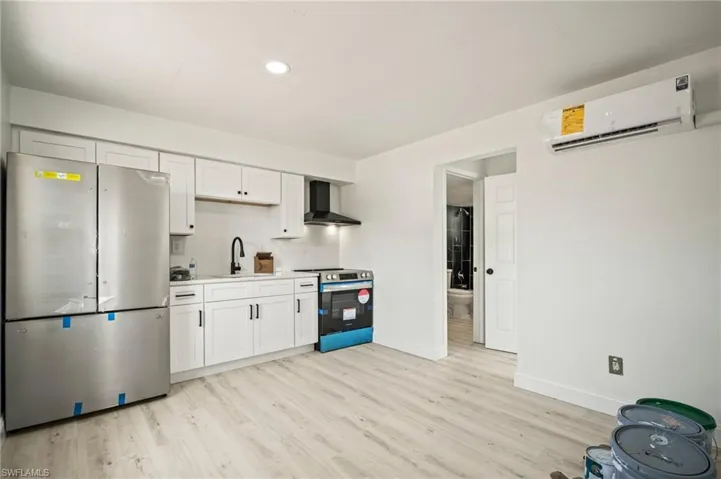 Kitchen featuring stainless steel appliances, a wall mounted air conditioner, wall chimney range hood, light wood-type flooring, and backsplash