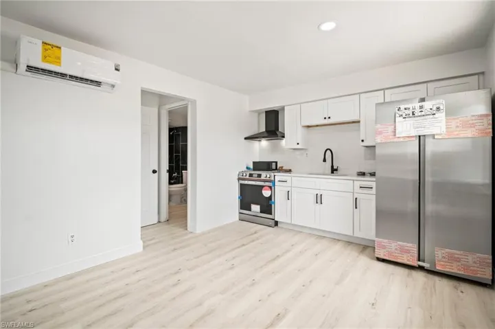 Kitchen featuring stainless steel appliances, wall chimney exhaust hood, a wall mounted AC, light wood-style flooring, and light countertops