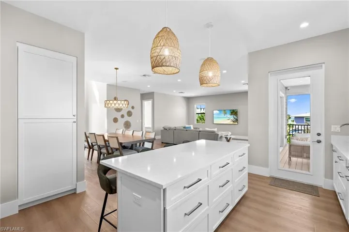 Kitchen with light wood-type flooring, recessed lighting, white cabinetry, a breakfast bar area, and hanging light fixtures. virtually edited photo