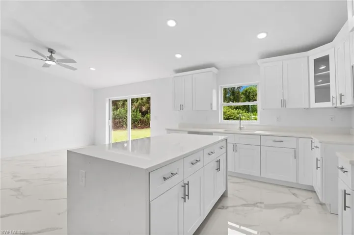 Kitchen featuring glass insert cabinets, white cabinetry, a center island, recessed lighting, and light stone countertops