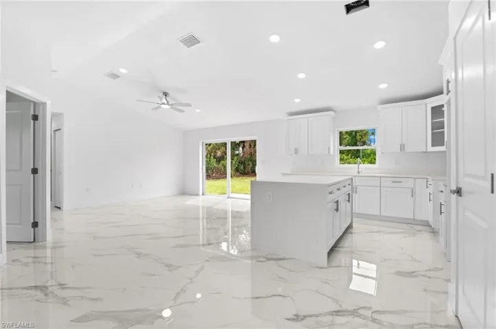 Kitchen with glass fronted cabinets, white cabinetry, recessed lighting, a center island, and ceiling fan