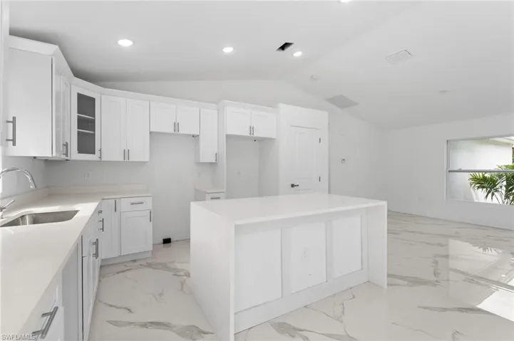 Kitchen featuring a kitchen island, glass insert cabinets, light stone counters, vaulted ceiling, and recessed lighting