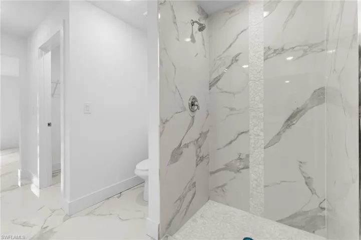 Full bath featuring a marble finish shower, a walk in closet, and light marble finish flooring