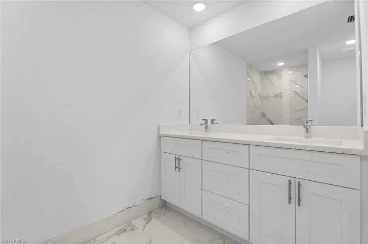Full bathroom featuring double vanity, light marble finish flooring, a marble finish shower, and recessed lighting