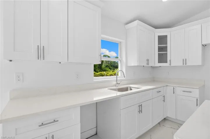 Kitchen featuring white cabinets, light stone countertops, light marble finish flooring, vaulted ceiling, and glass insert cabinets