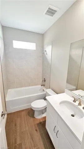 Full bathroom with vanity, tiled shower / bath combo, hardwood / wood-style flooring, and toilet