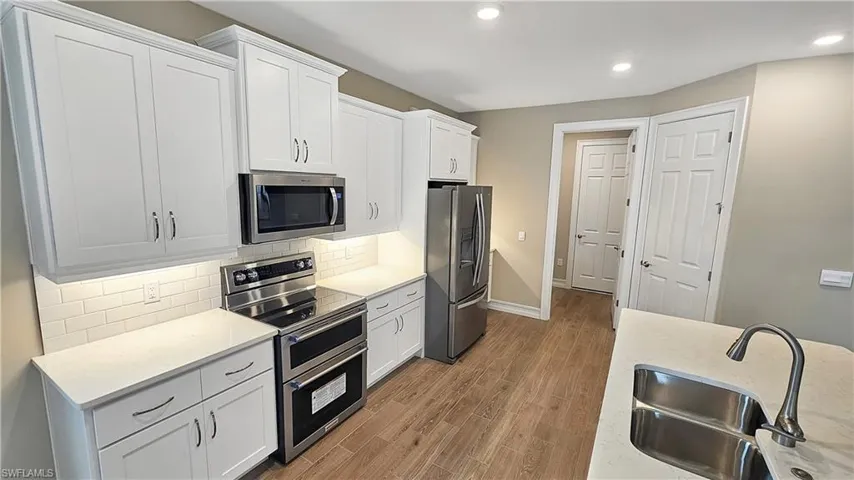 Kitchen featuring white cabinets, light wood-type flooring, sink, appliances with stainless steel finishes, and backsplash