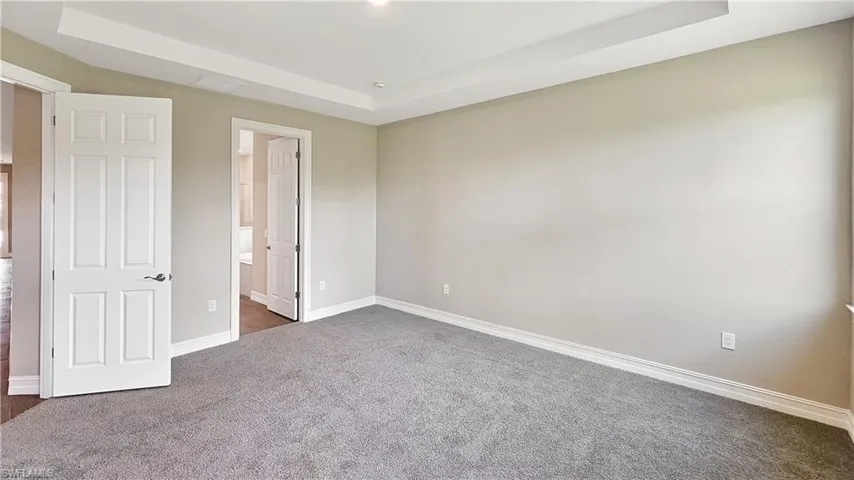Unfurnished bedroom with carpet floors, ensuite bath, and a raised ceiling