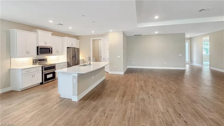 Kitchen featuring stainless steel appliances, white cabinets, sink, light hardwood / wood-style floors, and a kitchen island with sink
