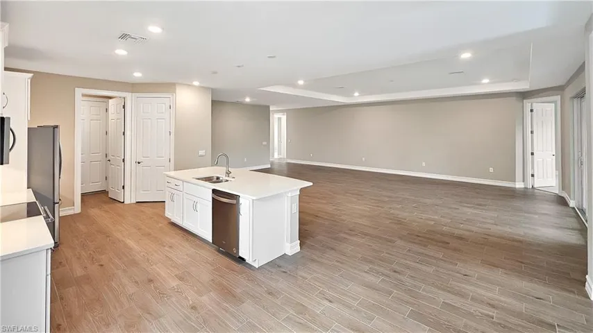 Kitchen featuring an island with sink, a tray ceiling, light hardwood / wood-style floors, appliances with stainless steel finishes, and sink
