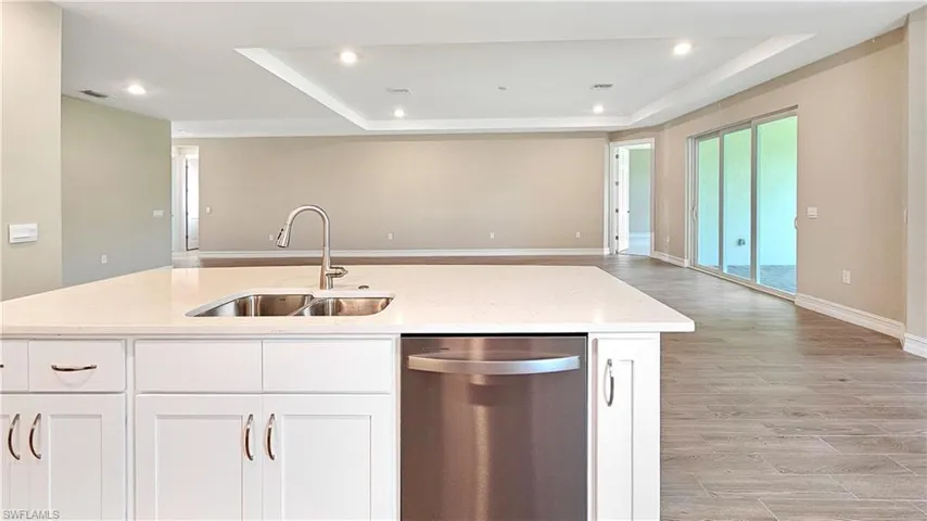 Kitchen featuring stainless steel dishwasher, a tray ceiling, an island with sink, sink, and light hardwood / wood-style flooring