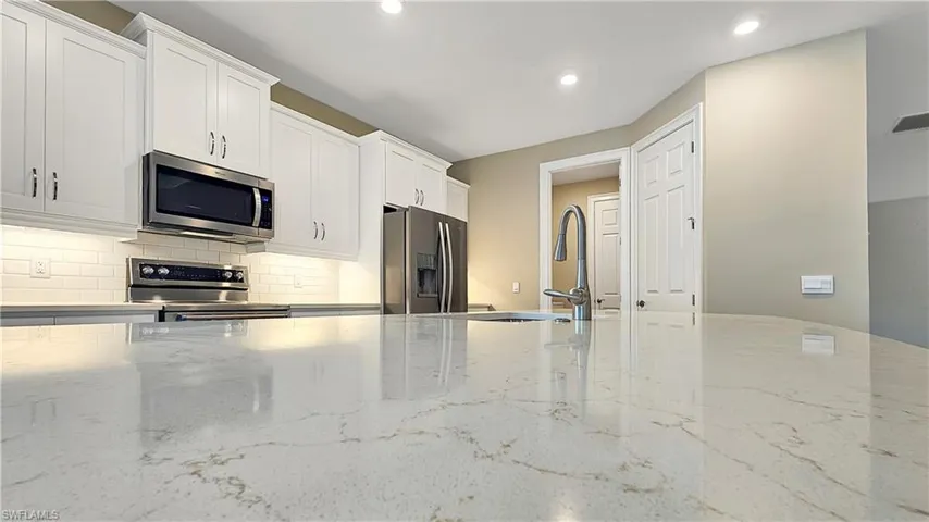Kitchen with light stone countertops, stainless steel appliances, backsplash, and white cabinets