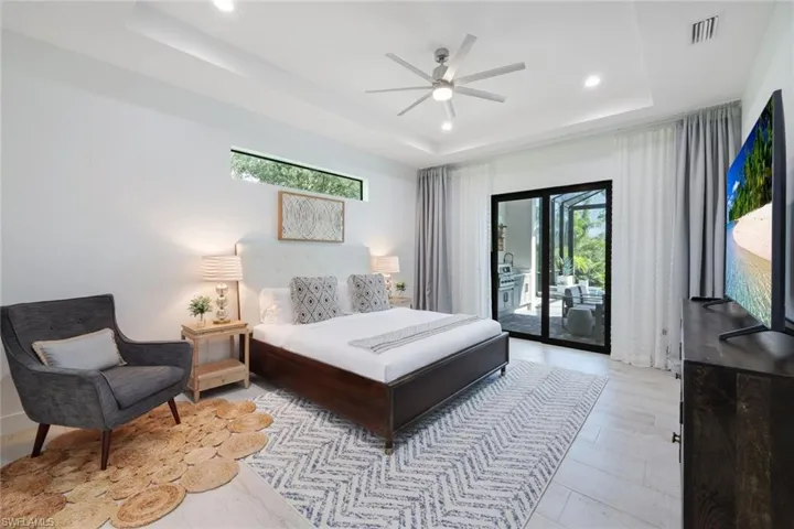 Bedroom with ceiling fan, a raised ceiling, access to exterior, and multiple windows