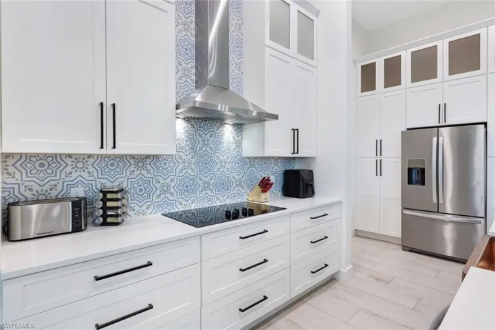 Kitchen featuring black electric cooktop, white cabinetry, backsplash, wall chimney range hood, and stainless steel fridge with ice dispenser