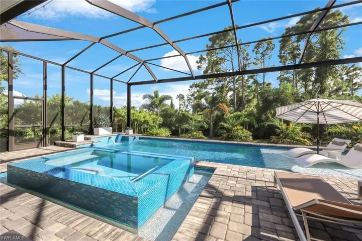 View of swimming pool with glass enclosure, an in ground hot tub, and a patio area