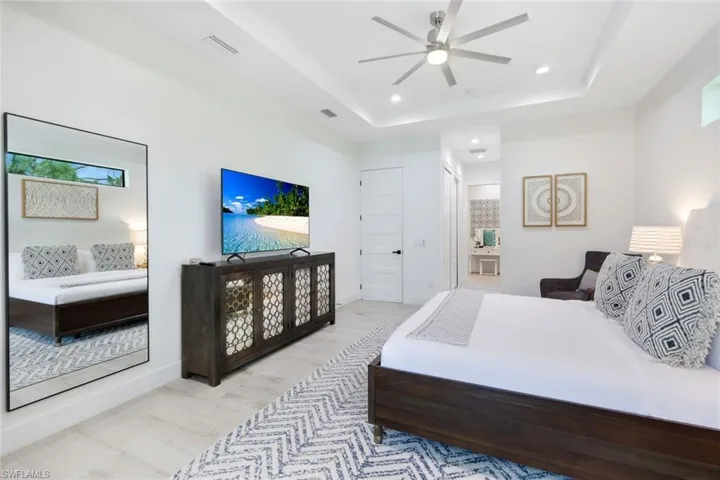 Bedroom featuring light hardwood / wood-style floors, ceiling fan, and a raised ceiling