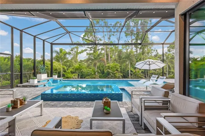 View of pool with glass enclosure, an in ground hot tub, and a patio area