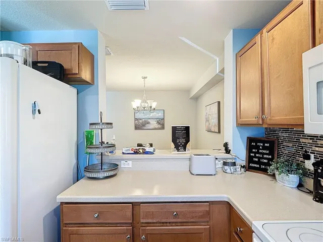Kitchen with white fridge, backsplash, a chandelier, and hanging light fixtures