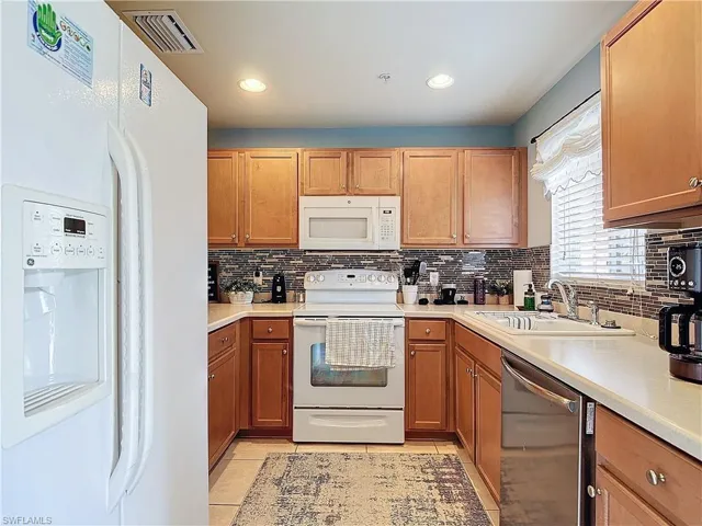 Kitchen featuring sink, light tile patterned floors, white appliances, and tasteful backsplash